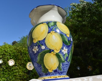 Può includere: Un vaso in ceramica blu e bianco con un motivo di limone giallo. Il vaso ha un'ampia apertura e una base stretta. È decorato con foglie verdi e fiori bianchi.