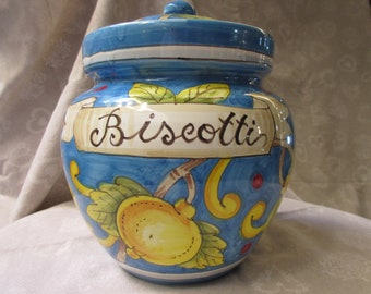 May include: A blue and white ceramic cookie jar with a yellow and green floral design. The jar has the word "Biscotti" written on it.