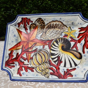 Könnte beinhalten: Eine rechteckige Servierplatte aus Keramik mit blauem Rand und weißem Hintergrund. Die Platte ist mit einem farbenfrohen Muschel-Design verziert, darunter rote Korallen, Seesterne und Muscheln.
