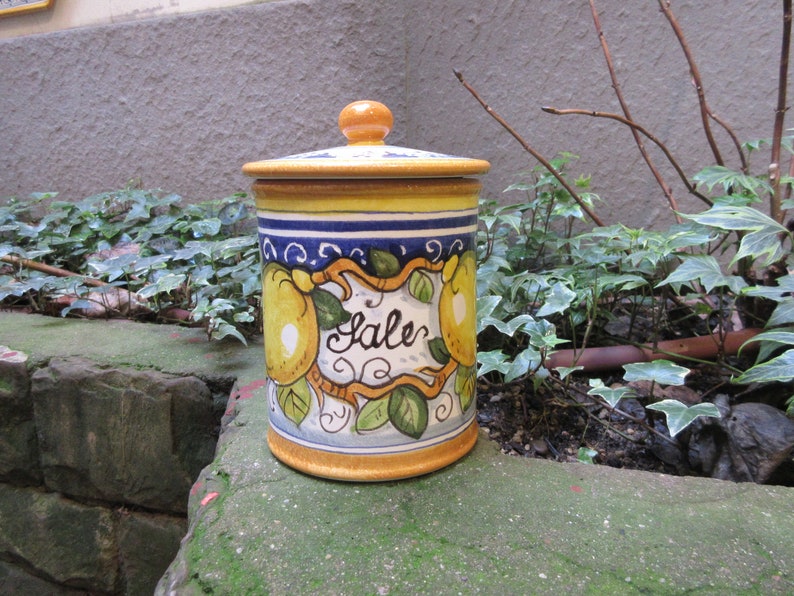 May include: A yellow, blue, and white ceramic jar with a lid. The jar has a lemon design and the word "Sale" written on it.