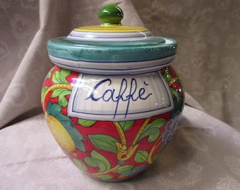 Op de afbeelding: Een keramische pot met een groen deksel en een rood, geel en groen bloemenontwerp. De pot is gelabeld met "Caffe" in cursief schrift.