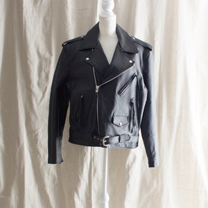 May include: A black leather motorcycle jacket with a zipper closure, a belt, and fringe details.