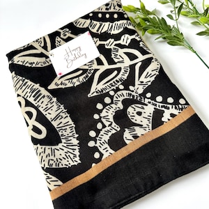 May include: Black and white patterned scarf with a tan border. The scarf has a floral design and the text "Happy Birthday" is written on a white tag.