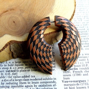 May include: A pair of wooden ear gauges with a geometric pattern in shades of brown and black. The gauges are round and have a slightly curved shape.