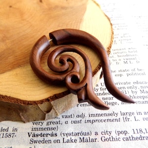 May include: A wooden ear gauge with a spiral design. The gauge is brown and has a natural wood finish.