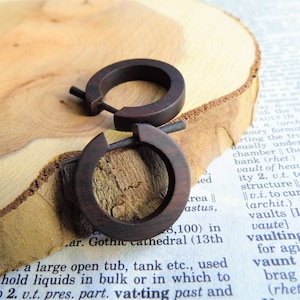 Könnte beinhalten: Ein Paar dunkelbraune Holz-Creolen. Die Ohrringe sind schlicht und elegant und würden jedes Outfit perfekt ergänzen.