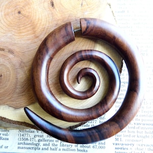 May include: A pair of brown wood spiral ear gauges. The gauges are made of a dark wood with a natural grain pattern. The gauges are in the shape of a spiral and are designed to be worn in the ear.