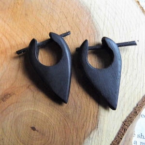 Könnte beinhalten: Ein Paar schwarze Holzohrringe in Tropfenform mit einem kleinen Ring. Die Ohrringe sind aus dunklem Holz gefertigt und haben eine glatte Oberfläche.