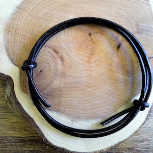 Könnte beinhalten: Ein schwarzes Lederband-Armband mit einem einfachen Knotendesign.