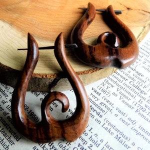 May include: A pair of wooden earrings with a unique, twisted design. The earrings are made of dark brown wood and have a natural, rustic look.