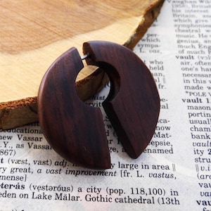 May include: A dark brown wooden earring with a unique split design. The earring is made of wood and has a natural finish.