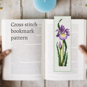 May include: Cross stitch bookmark pattern featuring a purple iris flower with green leaves and stems. The pattern is printed on white paper.