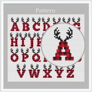 May include: A cross-stitch pattern featuring the alphabet from A to Z. Each letter is rendered in a red and black buffalo plaid design, topped with a pair of black antlers. A circular magnifying overlay highlights the letter A in detail.