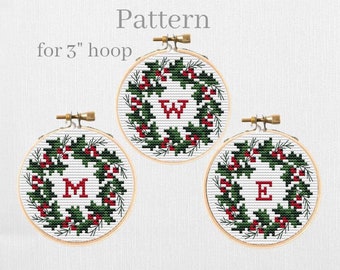 May include: Three 3-inch embroidery hoops with cross-stitch patterns of holly wreaths with red berries and a letter in the center. The letters are W, M, and E.