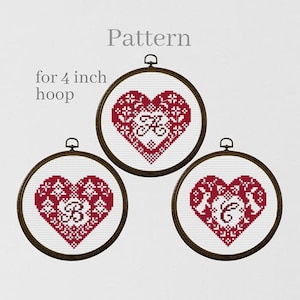 May include: Three cross-stitch patterns in wooden hoops, each featuring a red heart design with a letter. The text "Pattern" and "for 4 inch hoop" are visible. The hoops are displayed against a white background.