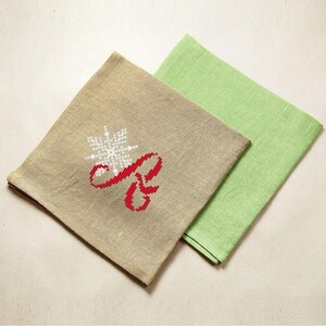 May include: Two fabric napkins, one beige with a red embroidered letter "R" and a white snowflake, and one green.