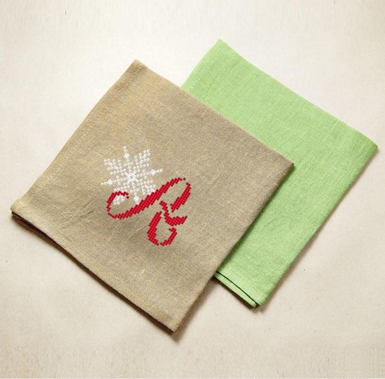 May include: Two fabric napkins, one beige with a red embroidered letter "R" and a white snowflake, and one green.