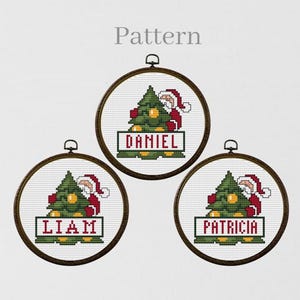 May include: Three round, wooden-framed embroidery hoops with cross-stitch designs of Santa Claus peeking out from behind a Christmas tree. Each hoop has a different name on a banner below the tree: Daniel, Liam, and Patricia.