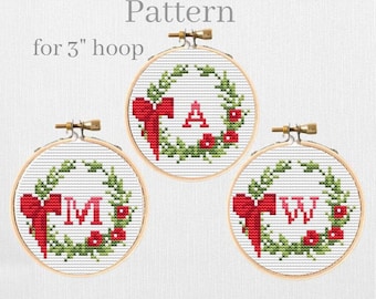 May include: Three embroidery hoops with a 3 inch diameter, each displaying a cross-stitch pattern of a Christmas wreath with a red bow and a letter in the center. The letters are A, M, and W.