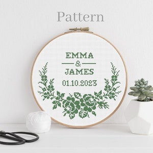 Puede incluir: Un aro de bordado blanco con un diseño floral verde y el texto "EMMA & JAMES 01.10.2023".