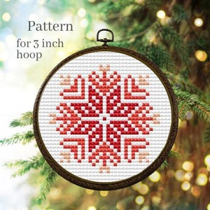 Puede incluir: Un patr&oacute;n de punto de cruz en un bastidor de 7,6 cm. El dise&ntilde;o presenta un copo de nieve rojo y blanco. El texto "Pattern for 3 inch hoop" es visible en la imagen. El bastidor tiene un marco de madera marr&oacute;n oscuro.