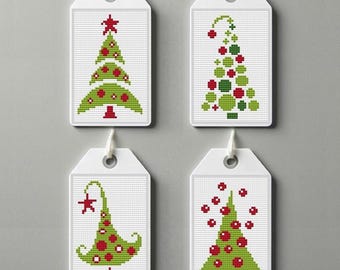 May include: Four white gift tags with different green and red Christmas tree designs. The trees are decorated with red ornaments and a star.