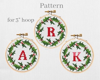 May include: Three 3-inch embroidery hoops with cross-stitch patterns of holly wreaths with red berries and a letter in the center. The letters are A, K, and R.