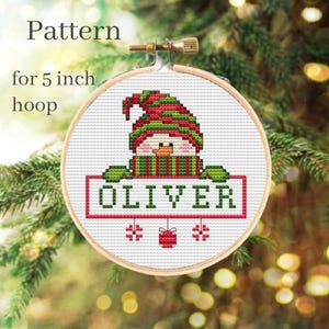 May include: Cross stitch pattern for a 5 inch hoop featuring a snowman wearing a red and green hat and scarf holding a sign that says "OLIVER".