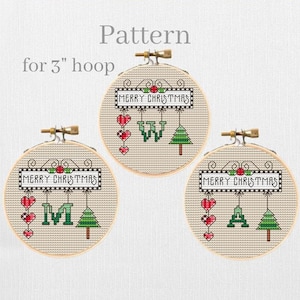 May include: Three 3-inch embroidery hoops with cross-stitch patterns for a Christmas ornament. Each hoop features a banner that says "Merry Christmas" with a red berry and a green holly leaf. The banner is hanging from a string with a red heart, a letter, and a green Christmas tree.