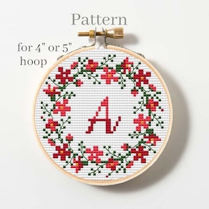 May include: Cross-stitch pattern in a wooden hoop. The design features a floral wreath with red flowers and green leaves surrounding the letter "A". The text "Pattern for 4" or 5" hoop" is at the top.