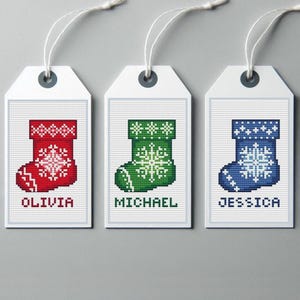 May include: Three white gift tags with red, green, and blue Christmas stockings with snowflakes. The tags are labeled "Olivia", "Michael", and "Jessica".
