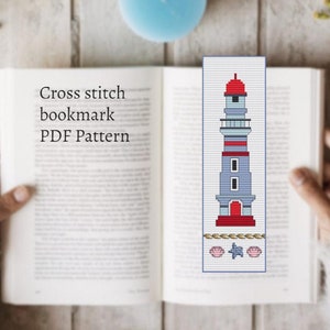 May include: Cross stitch bookmark PDF pattern featuring a lighthouse with a red roof, white trim, and blue walls. The lighthouse is surrounded by seashells and rope.