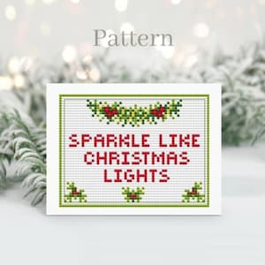 Patrón de punto de cruz con deseos navideños y tabla del alfabeto, tarjeta navideña pequeña con tabla ABC, luces navideñas brillantes.
