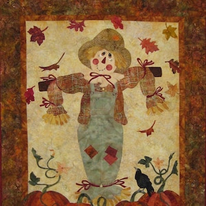 May include: A quilted wall hanging featuring a scarecrow with a straw hat, overalls, and a plaid shirt. The scarecrow is surrounded by pumpkins and fall leaves.