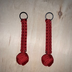 May include: Two red paracord keychains with black metal rings. The keychains have a round, knotted end.