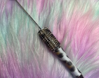 May include: A silver pen with a black and white animal print design and a clear crystal-encrusted top.