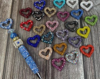 May include: A collection of colorful heart-shaped charms with rhinestones. The charms are made of metal and have a variety of colors, including red, blue, green, and purple.