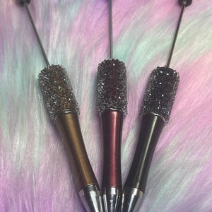 May include: Three sparkly pens with silver tops and different colored barrels: gold, burgundy, and black.