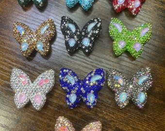 May include: Assortment of ten butterfly-shaped rhinestone embellishments in various colors, including green, blue, black, red, gold, silver, and pink.