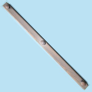 May include: A long, wooden shelf with three round, light brown knobs. The shelf is angled against a light blue background.