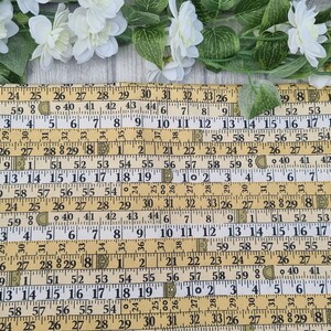 May include: A yellow and black fabric placemat with a repeating pattern of vintage measuring tapes. The numbers on the tapes are visible and include inches and fractions of an inch.