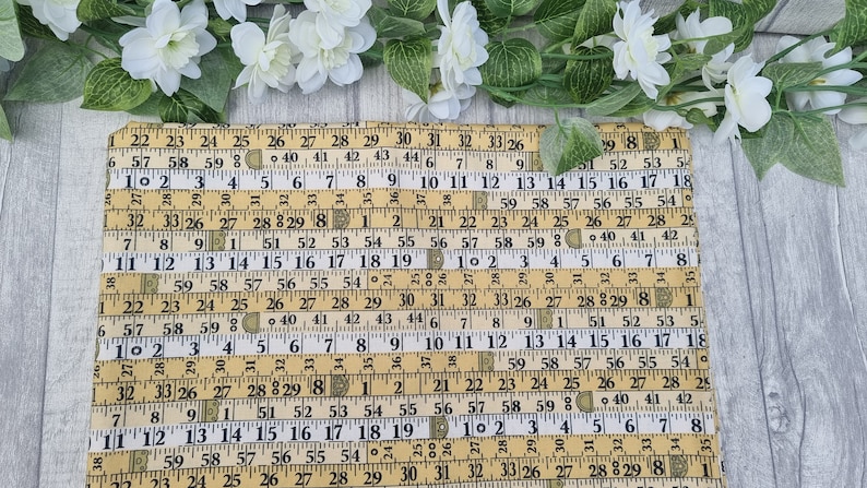 May include: A yellow and black fabric placemat with a repeating pattern of vintage measuring tapes. The numbers on the tapes are visible and include inches and fractions of an inch.