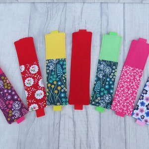 May include: Eight colorful fabric pencil holders with different floral patterns. The holders are made of two pieces of fabric sewn together, with a solid color on the top and a floral pattern on the bottom.