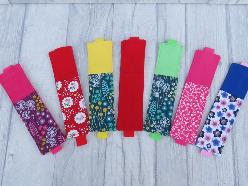 May include: Eight colorful fabric pencil holders with different floral patterns. The holders are made of two pieces of fabric sewn together, with a solid color on the top and a floral pattern on the bottom.