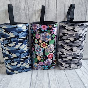Puede incluir: Tres bolsas de tela con diferentes patrones. La bolsa de la izquierda es de camuflaje azul y blanco. La bolsa del medio tiene un fondo negro con flores coloridas y calaveras de az&uacute;car. La bolsa de la derecha es de camuflaje gris y blanco.