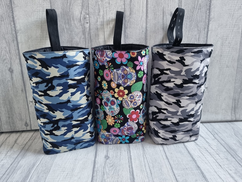 Puede incluir: Tres bolsas de tela con diferentes patrones. La bolsa de la izquierda es de camuflaje azul y blanco. La bolsa del medio tiene un fondo negro con flores coloridas y calaveras de az&uacute;car. La bolsa de la derecha es de camuflaje gris y blanco.
