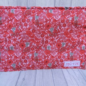 K&ouml;nnte beinhalten: Ein rosa-rotes Stoffkissen mit einem Blumenmuster und kleinen grauen Katzen. Das Kissen hat ein Etikett mit der Aufschrift "SYLVIE".