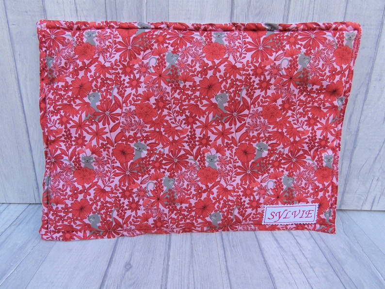 K&ouml;nnte beinhalten: Ein rosa-rotes Stoffkissen mit einem Blumenmuster und kleinen grauen Katzen. Das Kissen hat ein Etikett mit der Aufschrift "SYLVIE".