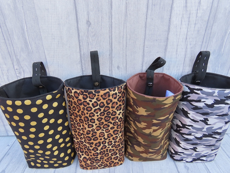 Puede incluir: Cuatro contenedores de almacenamiento de tela con asas negras y diferentes patrones. Los contenedores est&aacute;n alineados en una fila sobre un fondo de madera clara. Los patrones son lunares, estampado de leopardo, camuflaje y un patr&oacute;n de camuflaje gris y negro.