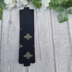 May include: Black fabric pencil case with a gold bee pattern. The case is closed and has a flap.